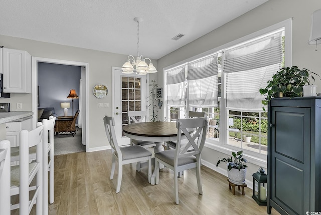 dining space with a chandelier, light wood finished floors, baseboards, and a textured ceiling