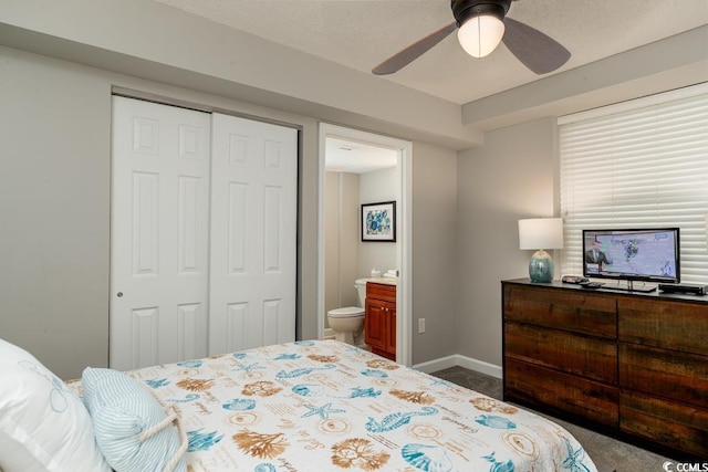 bedroom with dark colored carpet, a closet, baseboards, ensuite bathroom, and ceiling fan