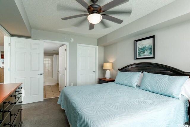 bedroom featuring dark colored carpet, ensuite bathroom, a textured ceiling, and a ceiling fan