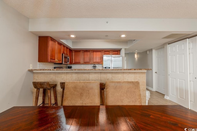1903 S Ocean Blvd S Unit 808, North Myrtle Beach, SC 29582 - kitchen with appliances with stainless steel finishes, a peninsula, backsplash, brown cabinetry, and light wood-type flooring