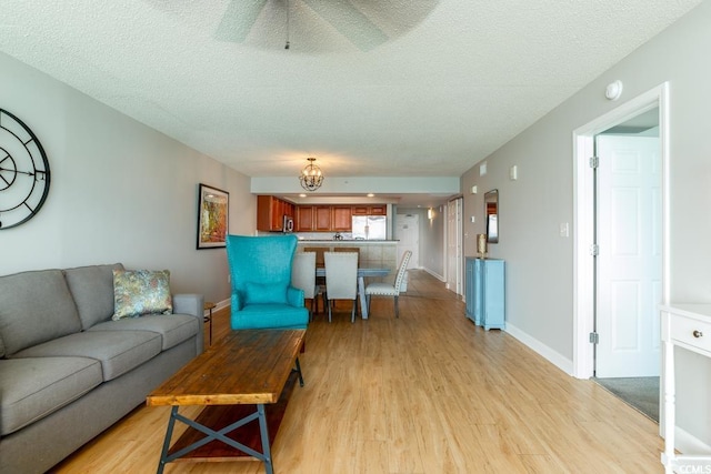 living area with light wood-style floors, a textured ceiling, baseboards, a chandelier, and a ceiling fan