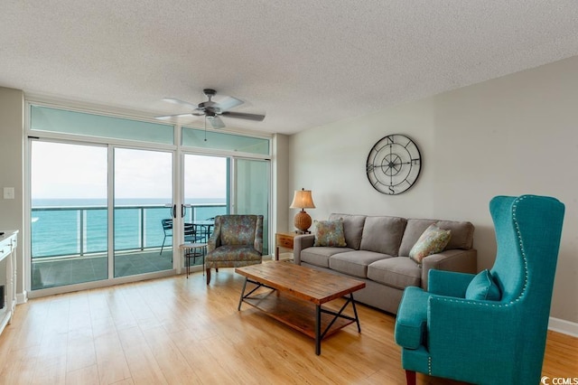 living area featuring a wall of windows, ceiling fan, a textured ceiling, light wood-style flooring, and a water view