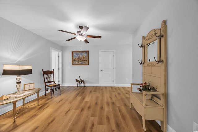 living area featuring baseboards, a ceiling fan, and light wood finished floors