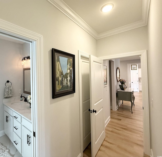 hallway featuring crown molding, a sink, light wood finished floors, and baseboards