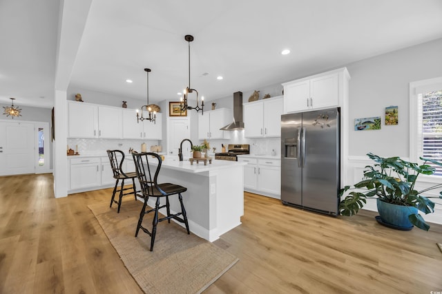 kitchen featuring stainless steel appliances, a chandelier, wall chimney exhaust hood, a kitchen bar, and tasteful backsplash