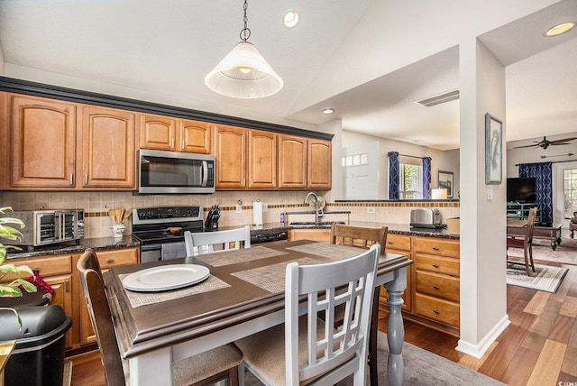 kitchen featuring stainless steel appliances, a sink, backsplash, dark wood-style flooring, and a ceiling fan