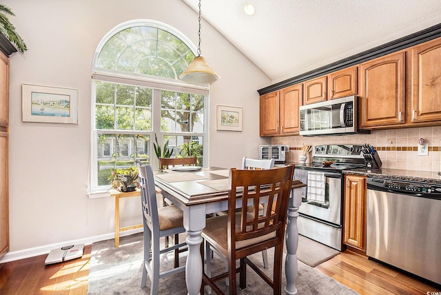 kitchen featuring appliances with stainless steel finishes, lofted ceiling, healthy amount of natural light, backsplash, and brown cabinets