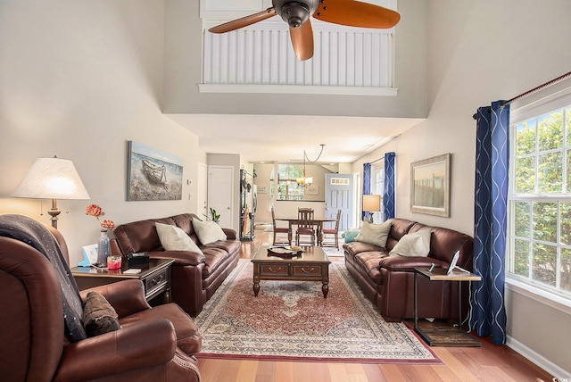 living area with plenty of natural light, ceiling fan, a chandelier, wood finished floors, and a high ceiling