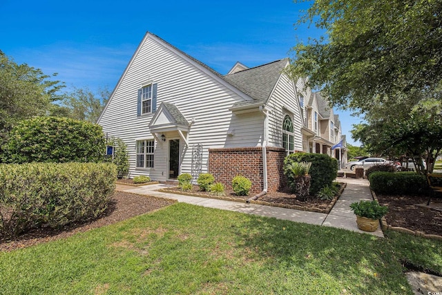 view of front facade featuring brick siding, a front yard, and a shingled roof