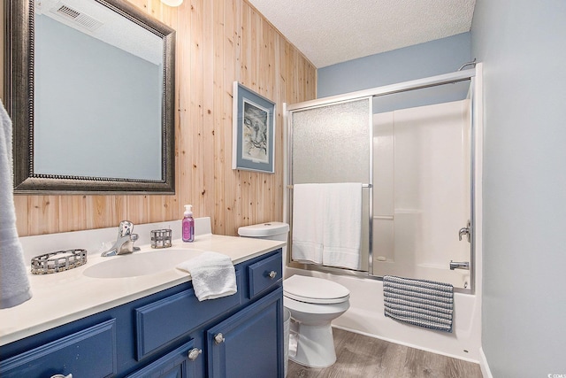 bathroom with wood walls, wood finished floors, vanity, toilet, and enclosed tub / shower combo