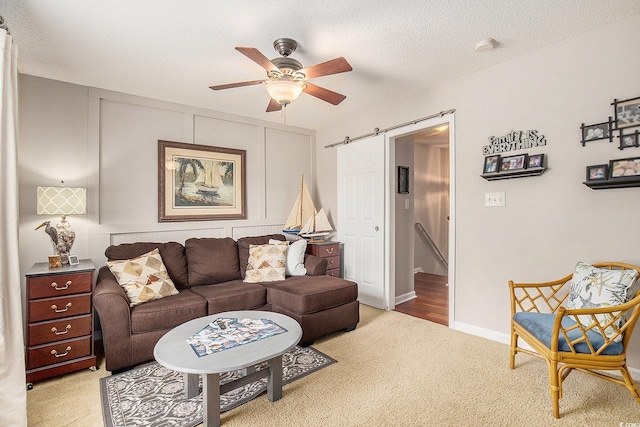 living room with light colored carpet, a ceiling fan, a barn door, and a textured ceiling
