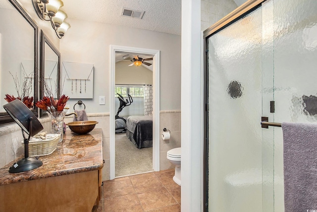full bathroom with connected bathroom, ceiling fan, toilet, a stall shower, and tile walls
