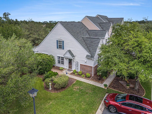 view of front of home with a shingled roof, a front yard, and brick siding