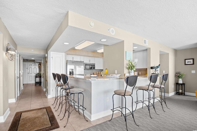 3805 S Ocean Blvd # 503, North Myrtle Beach, SC 29582 - kitchen featuring stainless steel appliances, a textured ceiling, a kitchen bar, white cabinetry, and a peninsula
