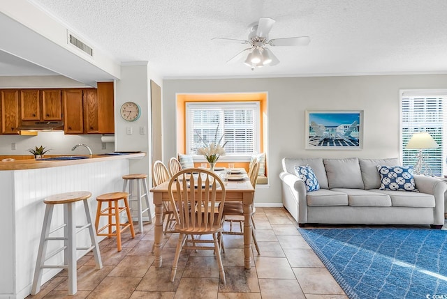 dining area featuring ceiling fan, a textured ceiling, ornamental molding, baseboards, and light tile patterned flooring