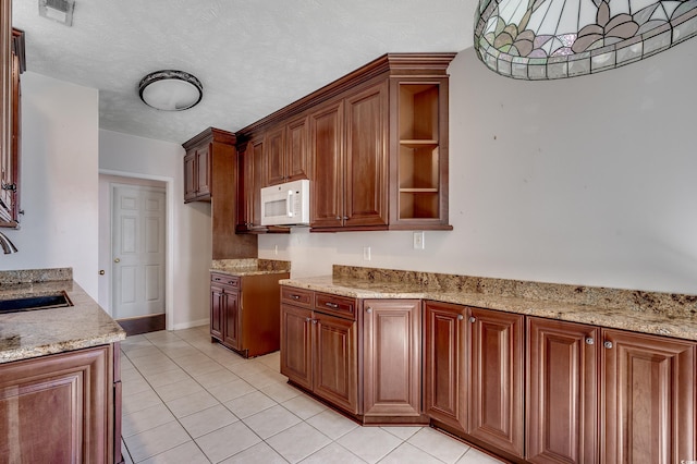 638 Hatteras River Rd, Myrtle Beach, SC 29588 - kitchen with white microwave, a sink, light tile patterned flooring, light stone counters, and brown cabinetry