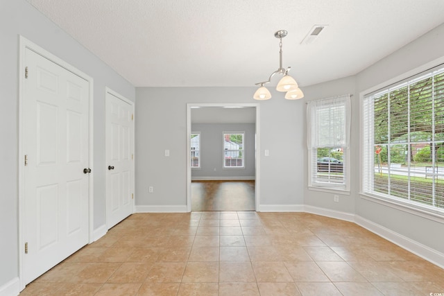 unfurnished dining area with a chandelier, light tile patterned flooring, baseboards, and a textured ceiling