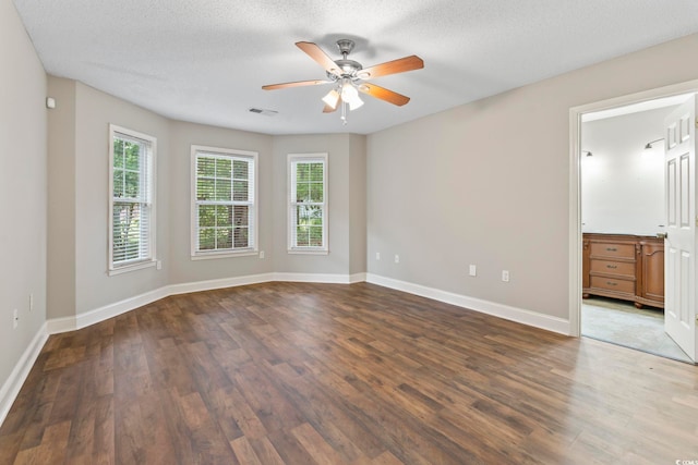 spare room featuring plenty of natural light, a ceiling fan, dark wood-style floors, baseboards, and a textured ceiling