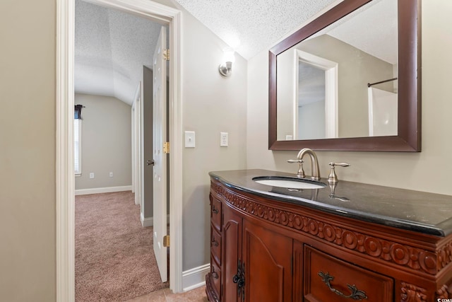 bathroom with vaulted ceiling, a textured ceiling, vanity, and baseboards