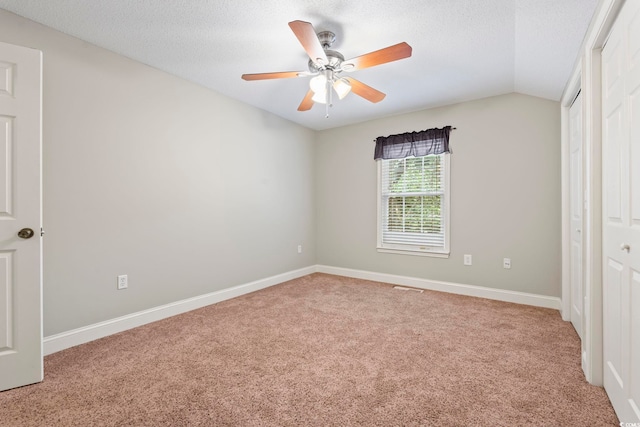 unfurnished bedroom featuring light colored carpet, a textured ceiling, vaulted ceiling, baseboards, and ceiling fan