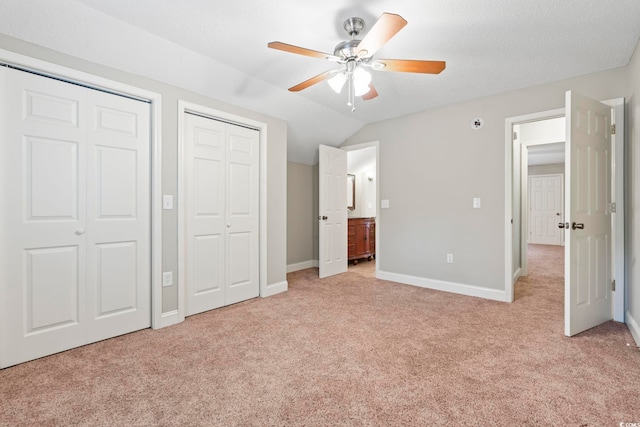 unfurnished bedroom with two closets, light carpet, vaulted ceiling, baseboards, and ensuite bathroom