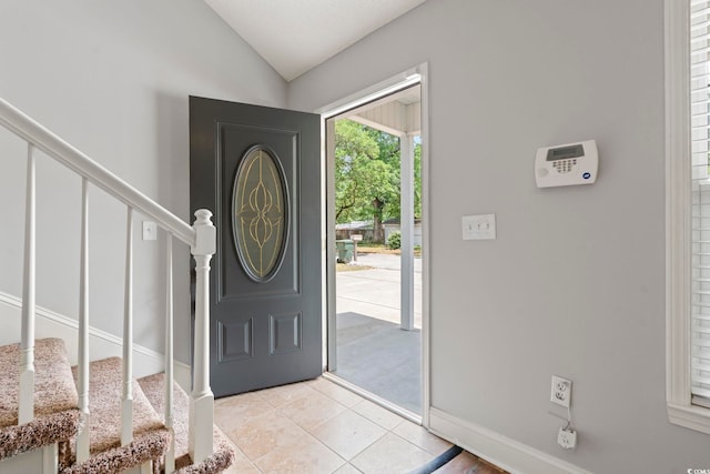 entryway with stairway, vaulted ceiling, light tile patterned floors, and baseboards