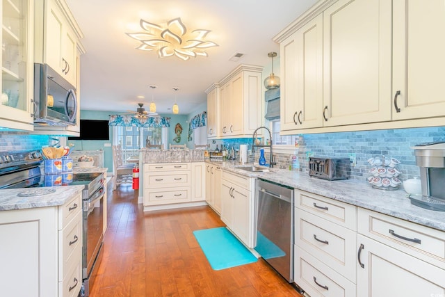 kitchen featuring stainless steel appliances, a sink, a peninsula, tasteful backsplash, and light wood-style floors