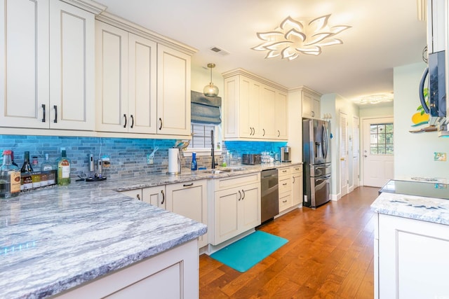 kitchen featuring stainless steel appliances, a sink, decorative backsplash, wood finished floors, and light stone countertops