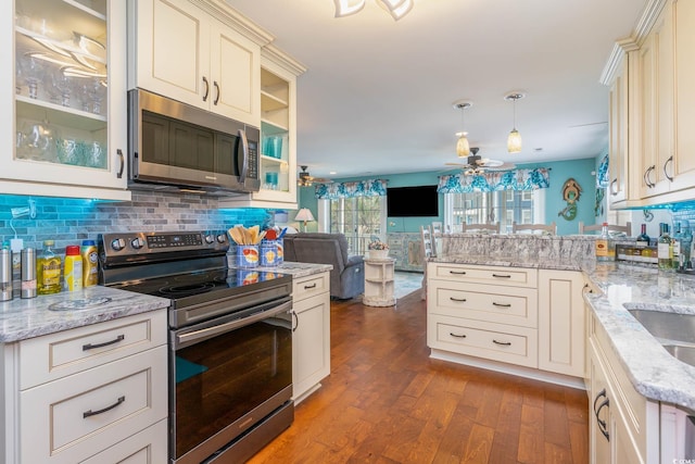 kitchen with appliances with stainless steel finishes, ceiling fan, a peninsula, dark wood-type flooring, and backsplash