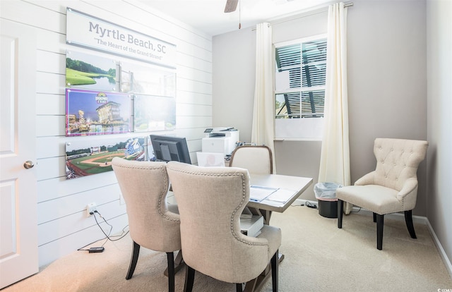carpeted home office featuring wood walls and a ceiling fan