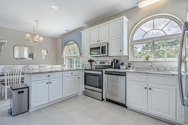 500 23rd Ave S, North Myrtle Beach, SC 29582 - kitchen with stainless steel appliances, a sink, a chandelier, white cabinetry, and a peninsula