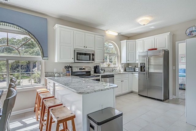 500 23rd Ave S, North Myrtle Beach, SC 29582 - kitchen featuring stainless steel appliances, a peninsula, white cabinetry, light stone countertops, and a textured ceiling