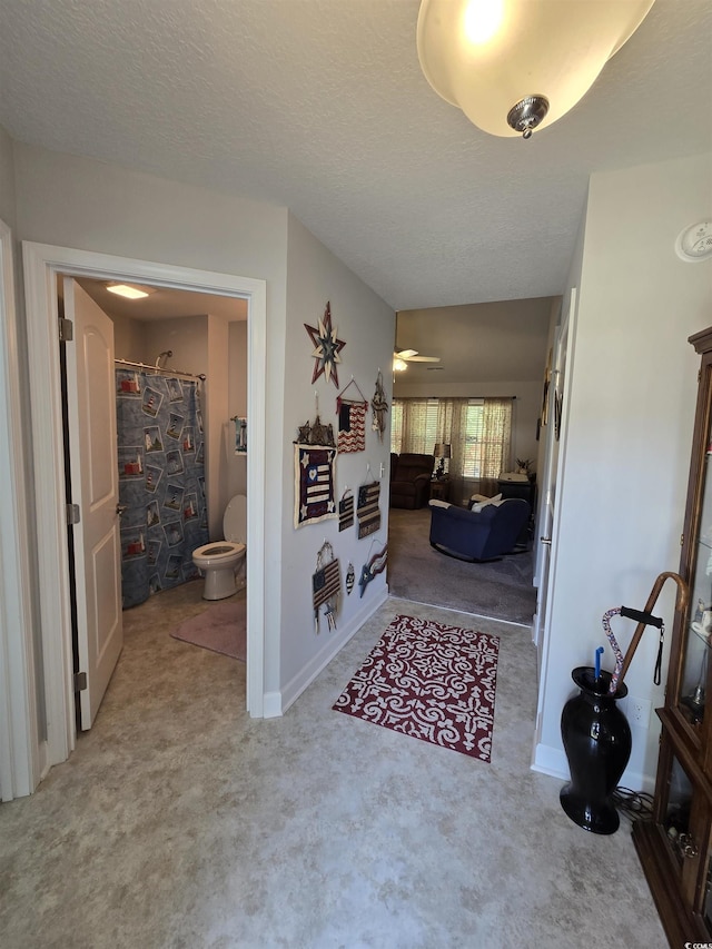 hallway featuring carpet flooring, baseboards, and a textured ceiling