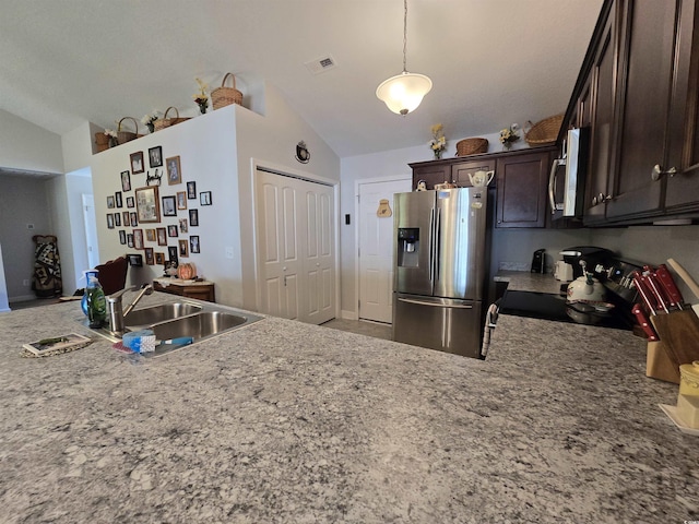 kitchen featuring appliances with stainless steel finishes, lofted ceiling, a sink, dark brown cabinets, and hanging light fixtures