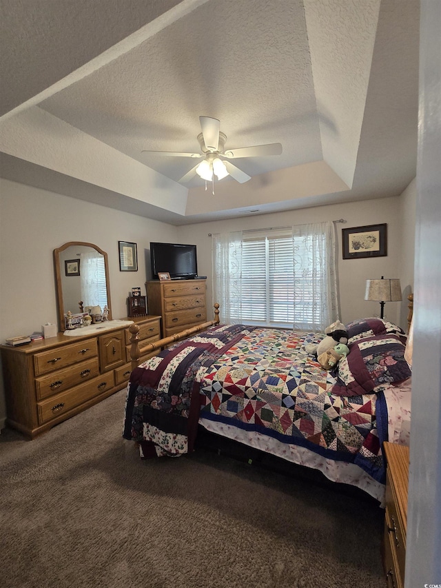 carpeted bedroom with a raised ceiling, a textured ceiling, and a ceiling fan