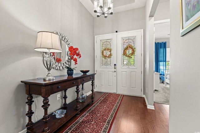 foyer entrance with wood finished floors, baseboards, a chandelier, and a towering ceiling