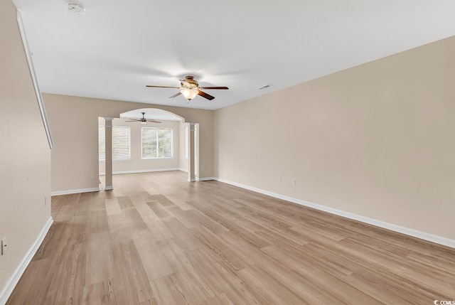 empty room featuring decorative columns, ceiling fan, a smoke detector, light wood finished floors, and baseboards