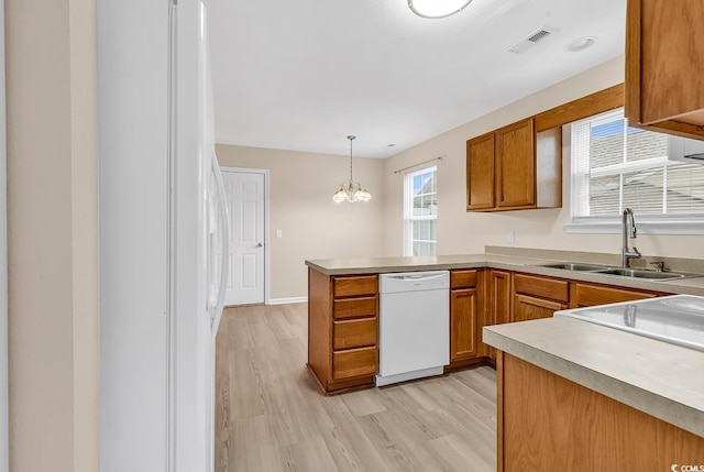 kitchen featuring white appliances, a sink, light wood-type flooring, a peninsula, and brown cabinetry