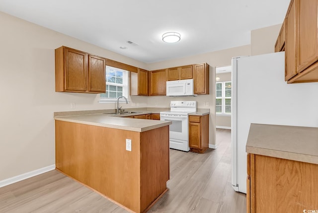 kitchen with white appliances, a sink, light wood-type flooring, and a peninsula