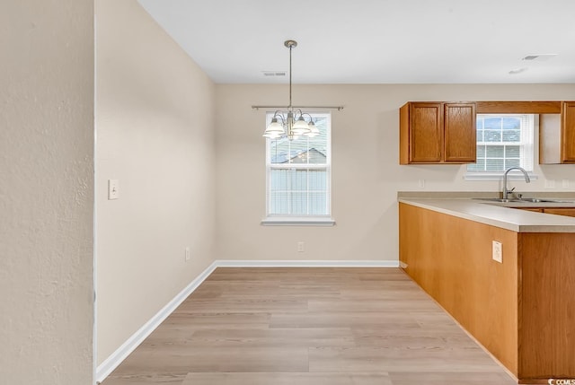 kitchen featuring a sink, brown cabinetry, light countertops, light wood-type flooring, and hanging light fixtures