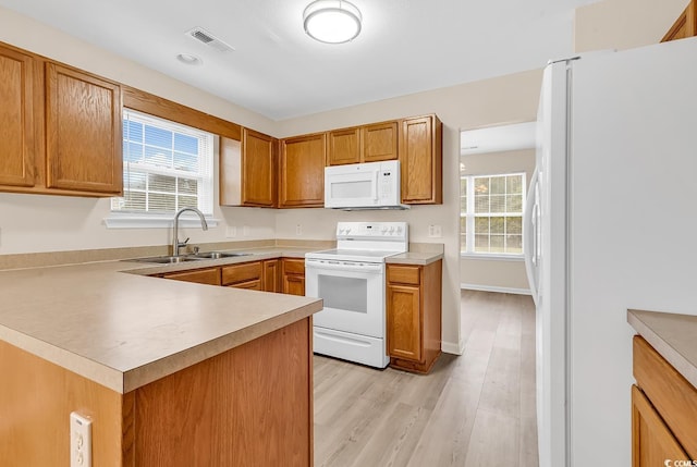 kitchen with white appliances, a sink, light wood-style floors, light countertops, and a peninsula