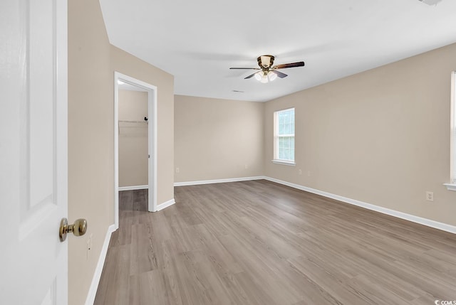 unfurnished bedroom with wood finished floors, baseboards, a walk in closet, and ceiling fan