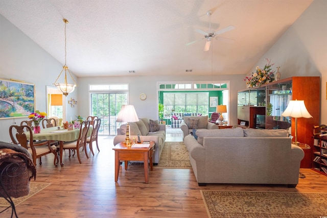 living area with wood finished floors, a ceiling fan, high vaulted ceiling, and a chandelier