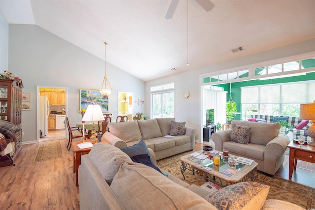 living room with light wood-type flooring, high vaulted ceiling, a ceiling fan, and a chandelier