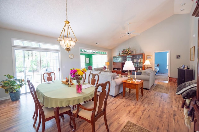 dining space with light wood finished floors, healthy amount of natural light, ceiling fan, high vaulted ceiling, and baseboards