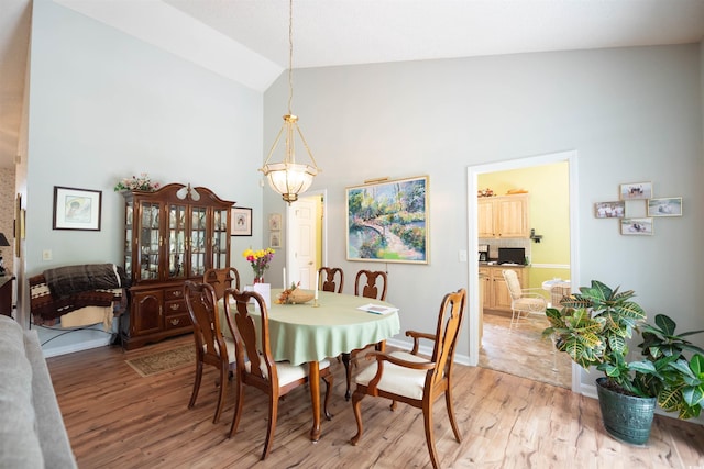dining space featuring high vaulted ceiling, light wood-type flooring, baseboards, and a chandelier