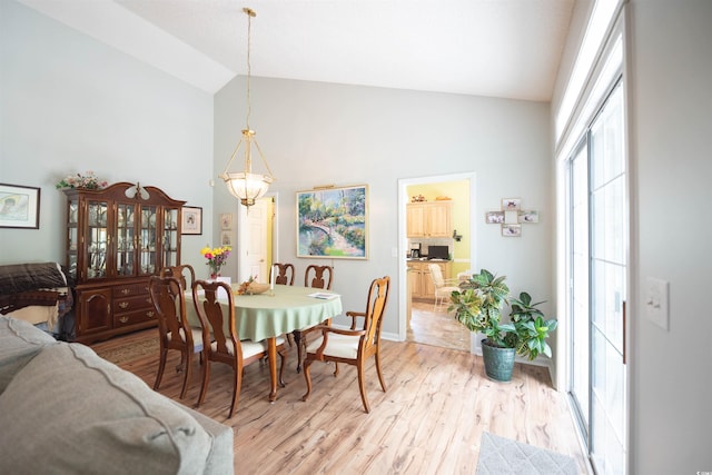 dining area featuring light wood finished floors, a chandelier, baseboards, and high vaulted ceiling