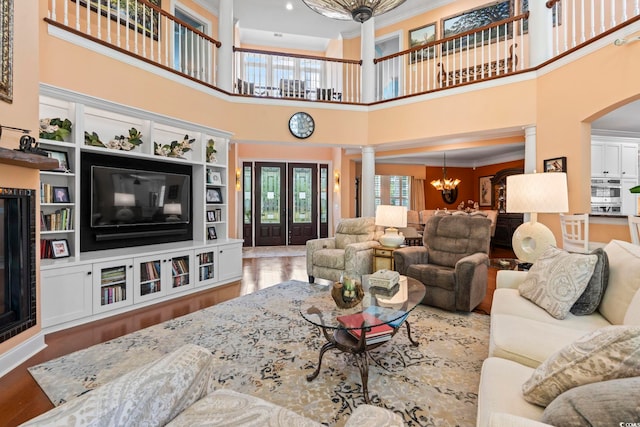 living room featuring decorative columns, a chandelier, a high ceiling, wood finished floors, and ornamental molding