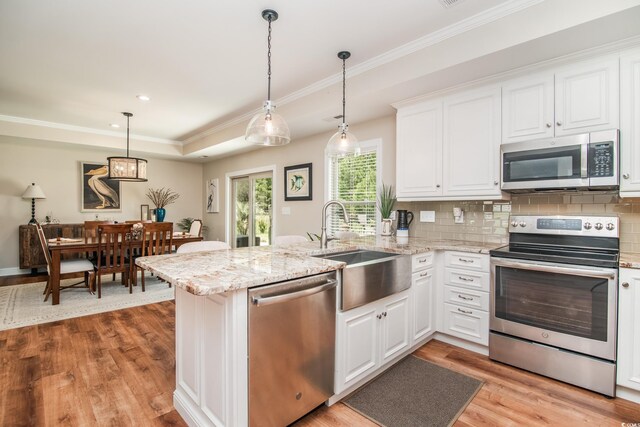 kitchen with stainless steel appliances, a sink, a peninsula, light wood-style flooring, and white cabinets