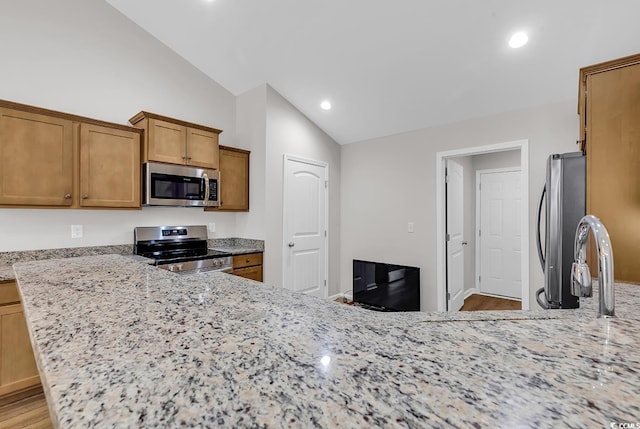 kitchen with appliances with stainless steel finishes, lofted ceiling, brown cabinetry, light wood-style flooring, and light stone counters